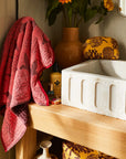A pink and red piping edge hand towel with a wavy end on both sides.