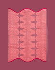 A pink and red piping edge hand towel with a wavy end on both sides.