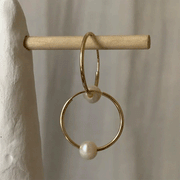On a tan background is a pair of gold hoop earrings with a pearl on the bottom of each hoop.