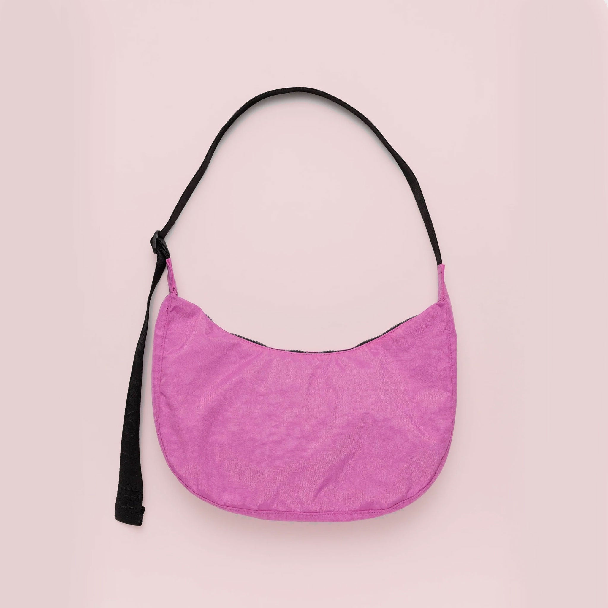 On a pink background is a hot pink crescent shaped nylon handbag with a black strap. 