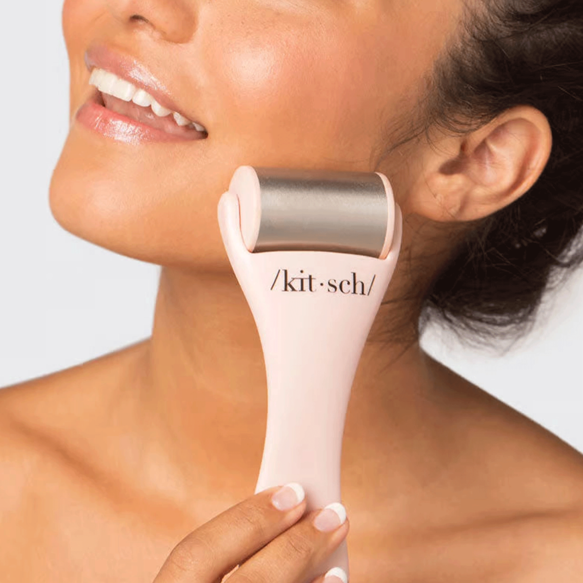 On a white background is a model holding a light pink and stainless steel facial ice roller.