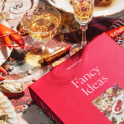 A red puzzle that showed the photo of the finished puzzle that is a elaborate table filled with lobster, cocktail glasses, seafood and olives with text that reads, 'Fancy Ideas Piecework Puzzles'.