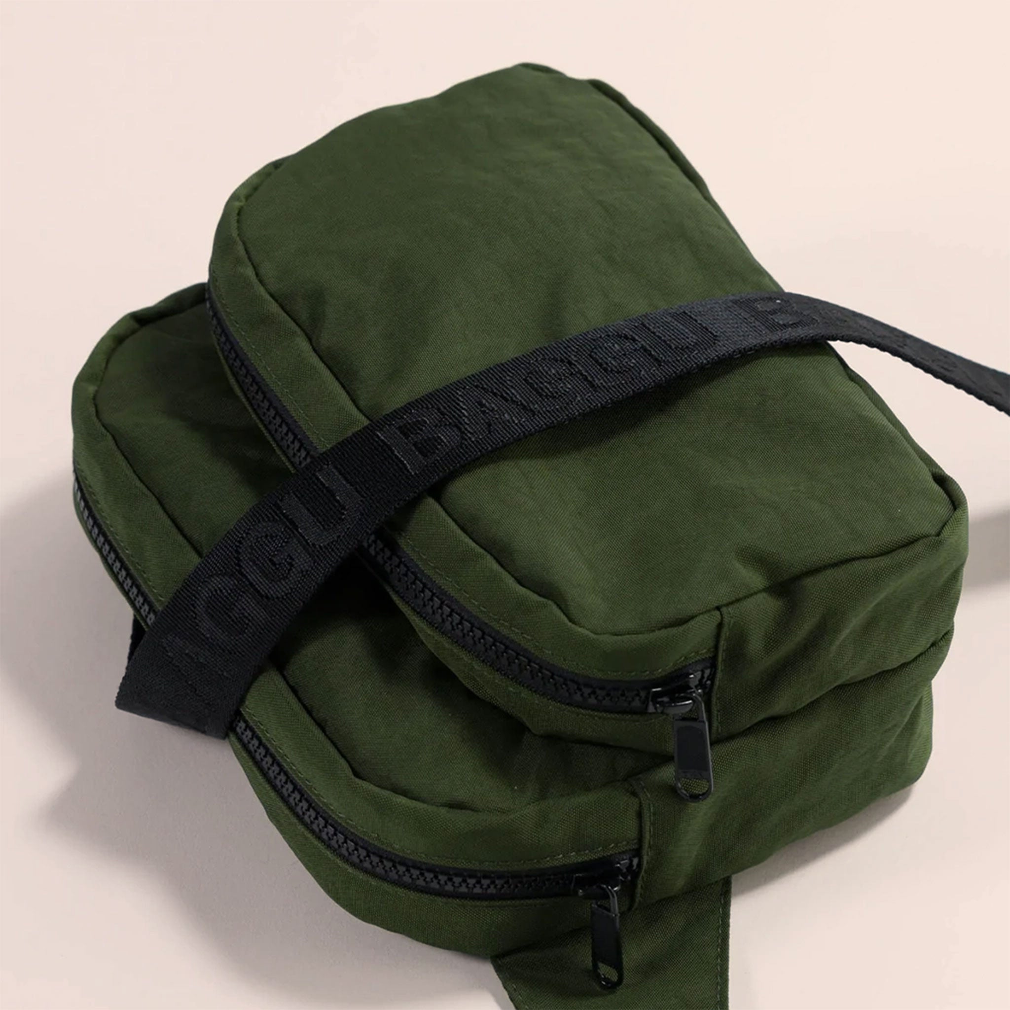 A dark green nylon fanny pack with two zipper pockets and a black adjustable strap.