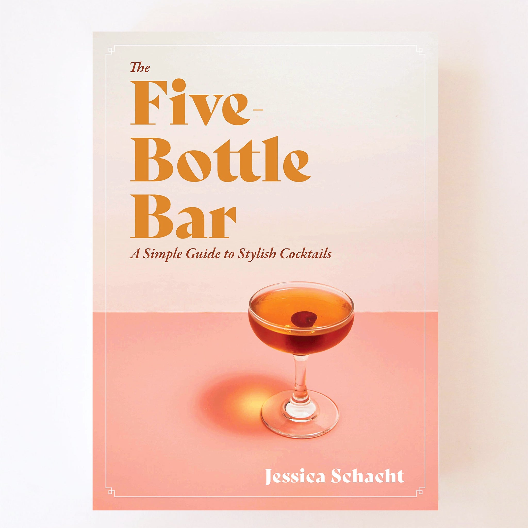 A cream and light pink book cover with a photograph of a coupe cocktail glass filled with an orange liquid along with orange text in the top left corner that reads, &quot;The Five Bottle Bar, A Simple Guide to Stylish Cocktails&quot;.