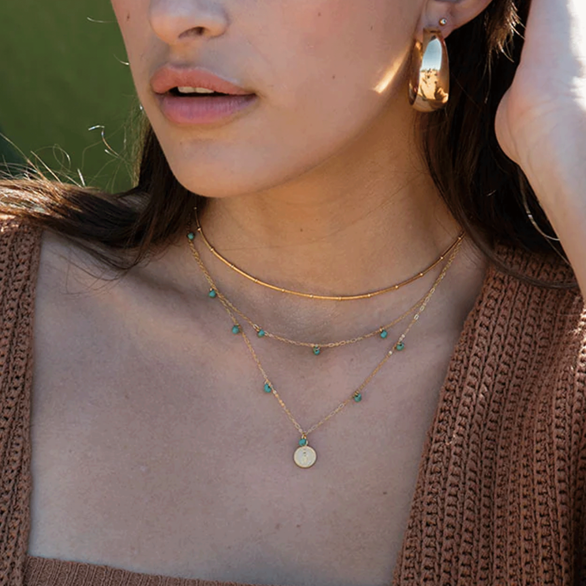 A gold dainty chain necklace with five turquoise beads spaced out along the chain layered here with other necklaces and worn on a model.