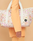 On an orange background is a floral printed tote bag with an ivory strap.