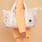 On an orange background is a floral printed tote bag with an ivory strap.