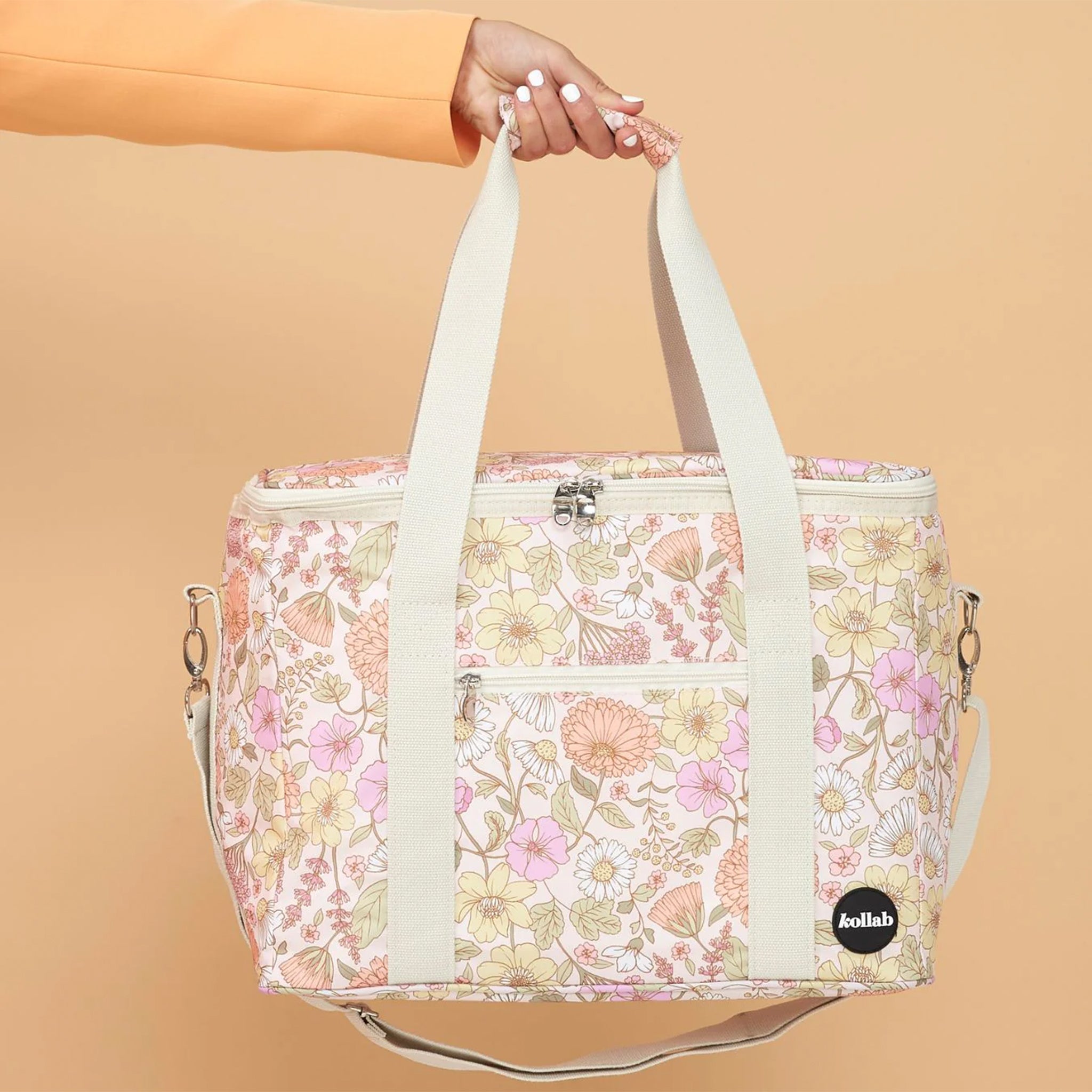 An ivory, floral print picnic bag with white straps and zippers.