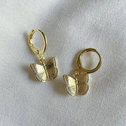 A pair of gold huggie earrings with butterfly charms.