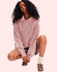 A dusty rose colored cable knit sweater worn on a model.