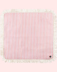 A coral and ivory stripe picnic mat with a fringe edge and a buckle for folding.