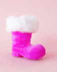 A fuscia velvet Santa boot ornament with white fur sits on a pink background.