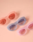On a peachy background is a group photo of three of the different color options for the Gemma Sunglass frame shape.