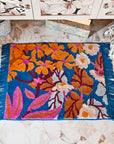 Blue bath mat with blue fringe, with orange, pink and white flowers.