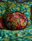 A maroon and multi colored floral round pillow with a fringe edge.