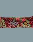 Long red velvet cushion with a colorful floral print and olive green tassels.