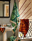 A green floral print towel with cream tassels on each end.