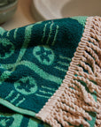 A green floral print hand towel with cream tassel details on two ends.