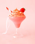 A pink and clear cocktail shaped ornament with a whipped topping and a red and white striped straw with a ribbon loop for hanging.