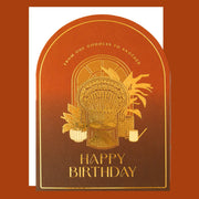 Greeting card with wicker chair, plants, and 'Happy Birthday' text on a brown background