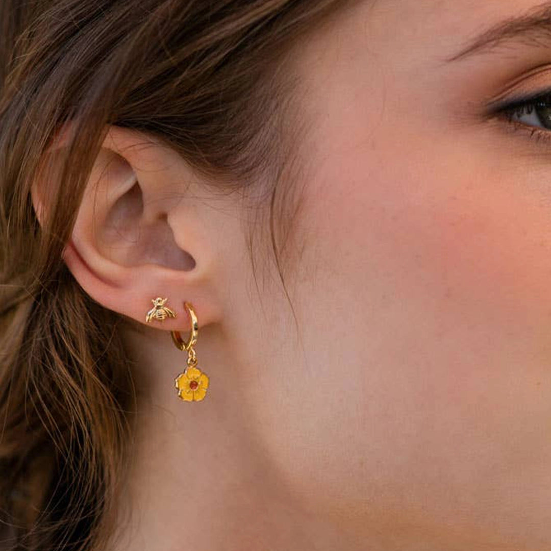A model wearing a pair of gold stud earrings in the shape of a honey bee.