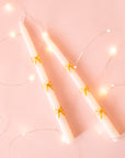 A pair of ivory taper candles with a gold bow design.