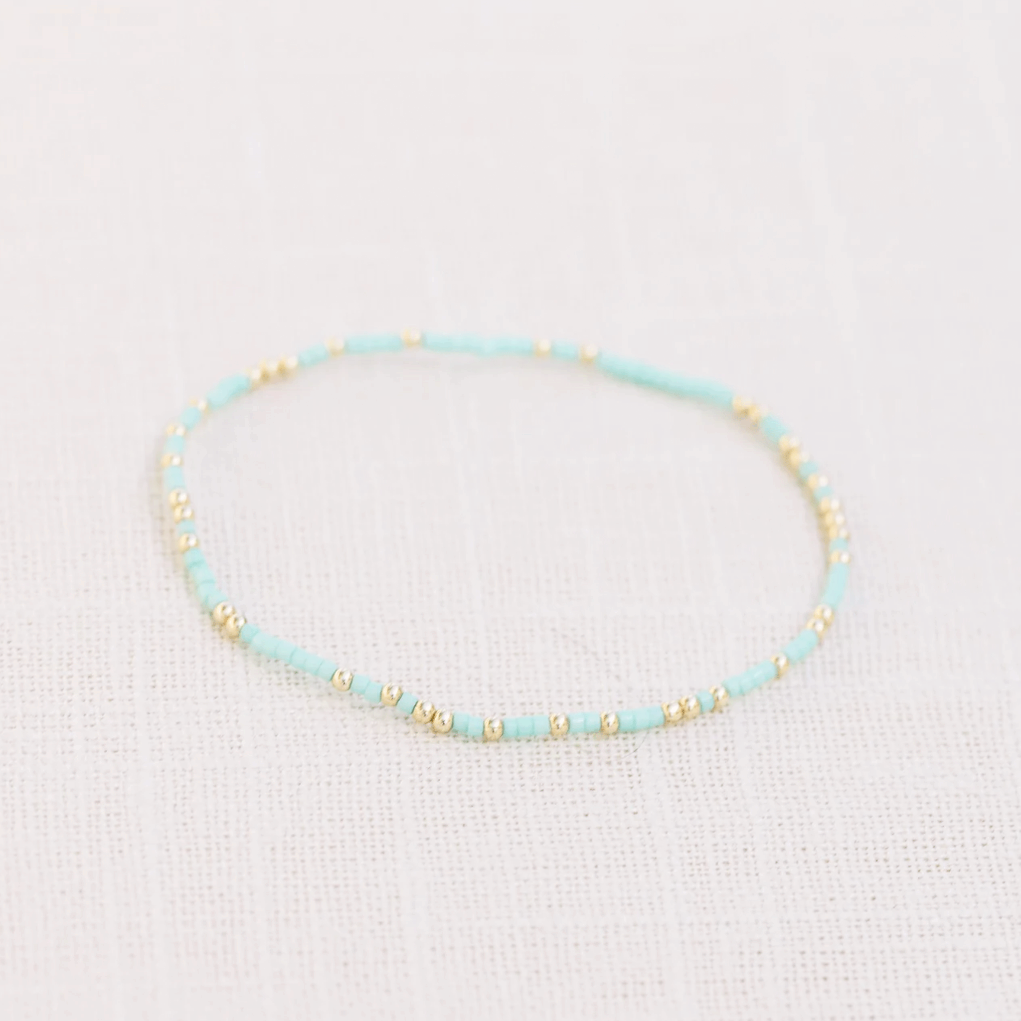 On a white background isa teal and gold bead bracelet. 