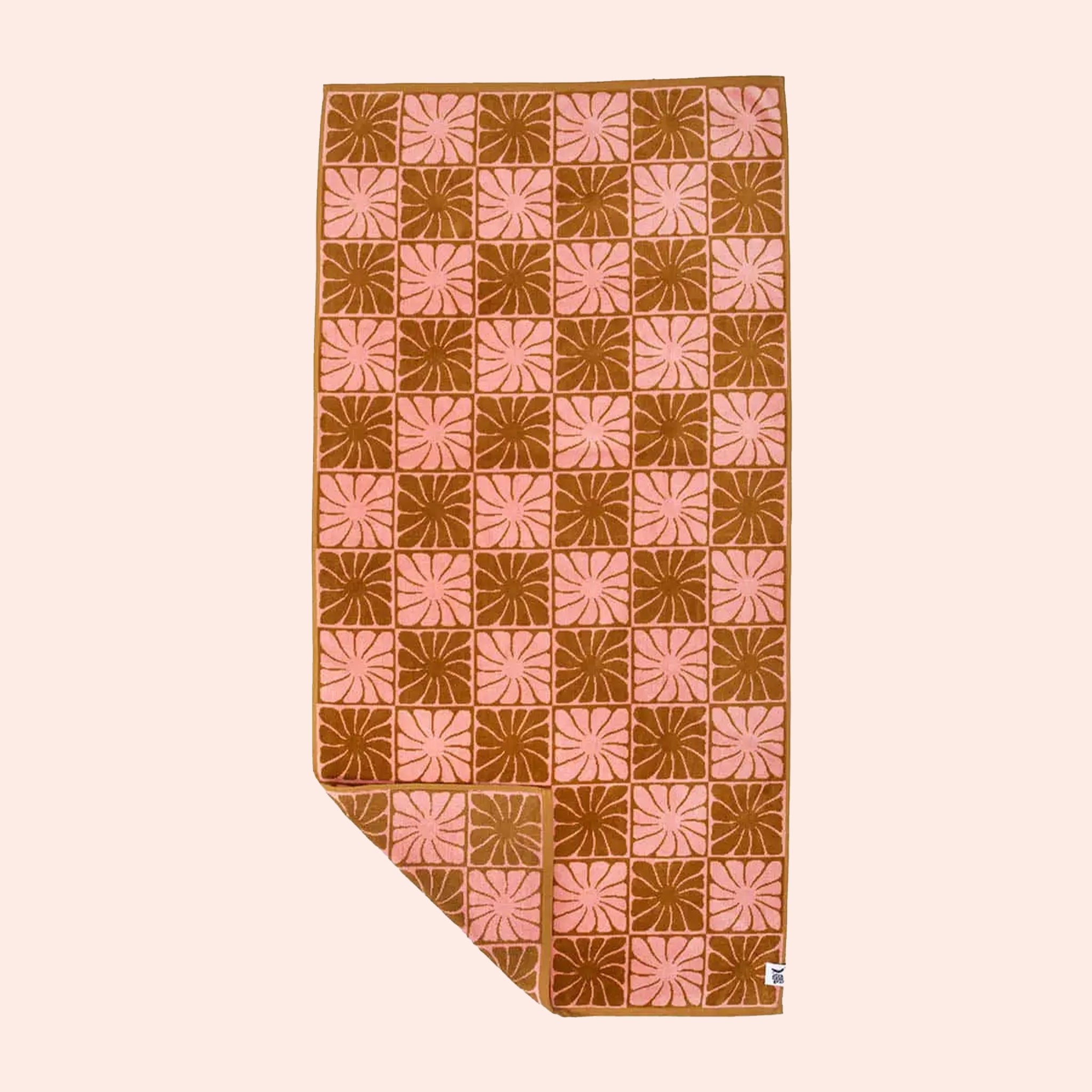 On a cream background is a pink and burnt orange bath/beach towel with a wavy floral checker design in each of the squares. 