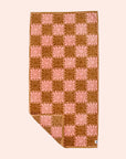 On a cream background is a pink and burnt orange bath/beach towel with a wavy floral checker design in each of the squares.
