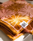 A pink and burnt orange bath/beach towel with a wavy floral checker design in each of the squares photographed here folded on a counter.