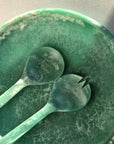 A green resin shallow serving bowl with a set of salad servers.