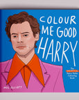 On a grey background is a blue coloring book cover with an illustration of Harry Styles and text that reads, "Colour Me Good Harry".