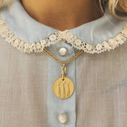 A large gold coin pendant necklace on a chain. The pendant has a fish tail design.