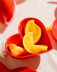 A red ceramic heart shaped bowl holding sliced oranges.