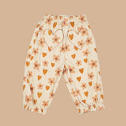 A pair of neutral kids pants with an orange heart and floral print and heart shaped pockets.