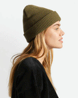 An olive green knit beanie with plush acrylic and has a folding cuff detailed with a woven label.
