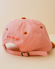 A light pink and orange baseball cap with an orange embroidered hibiscus flower in the center.