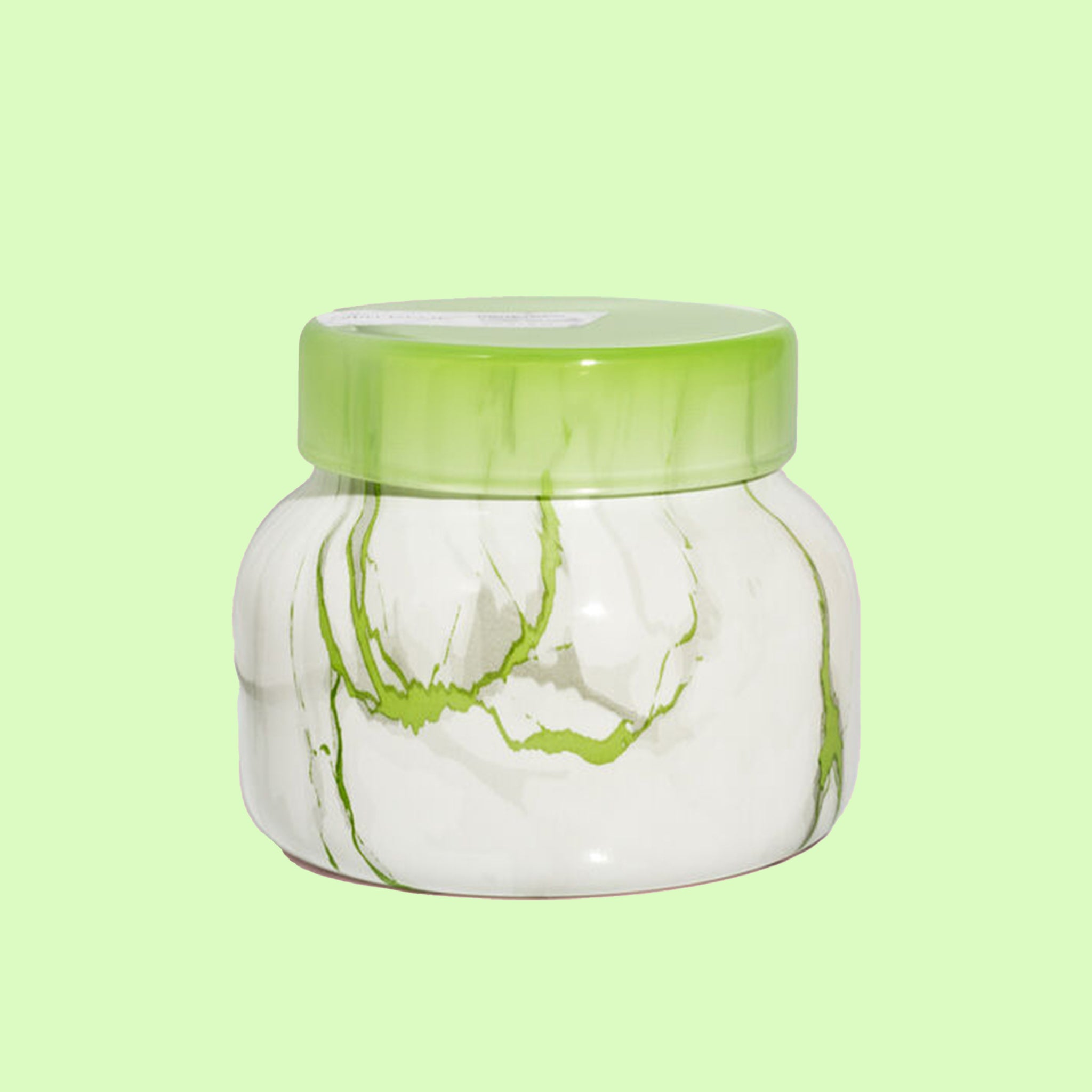 On a green background is a green and white marble jar candle with a lid.
