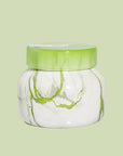 On a green background is a green and white marble jar candle with a lid.