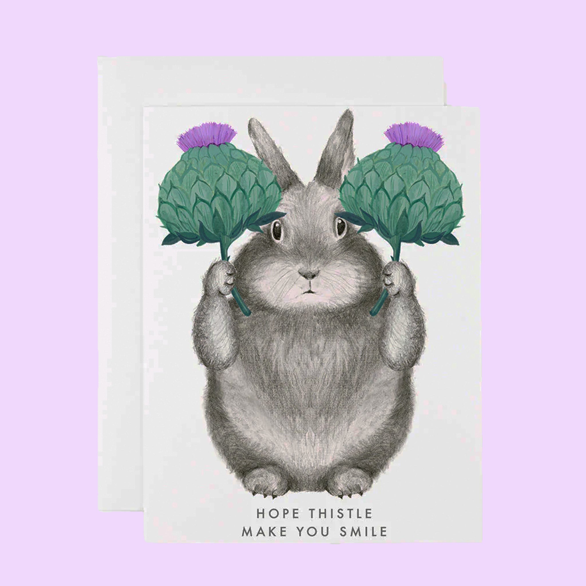 A white card with a grey bunny illustration holding two bundles of thistle and text below that reads, "Hope Thistle Make You Smile". 