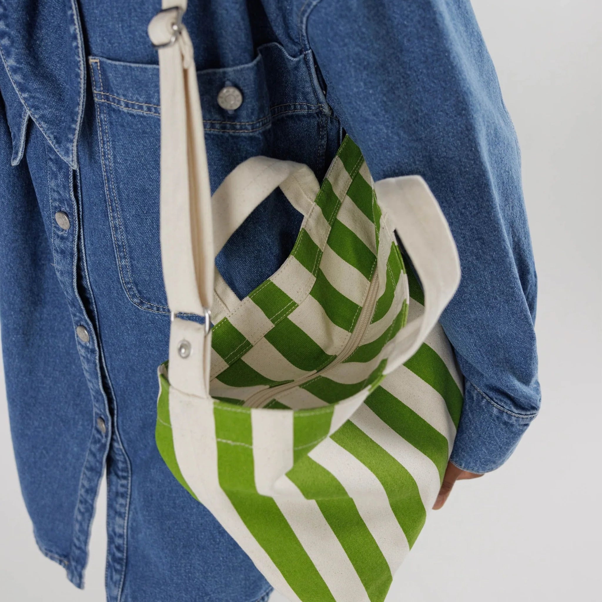 On a white background is a green and white canvas tote bag with two hand straps and one larger over the shoulder option.