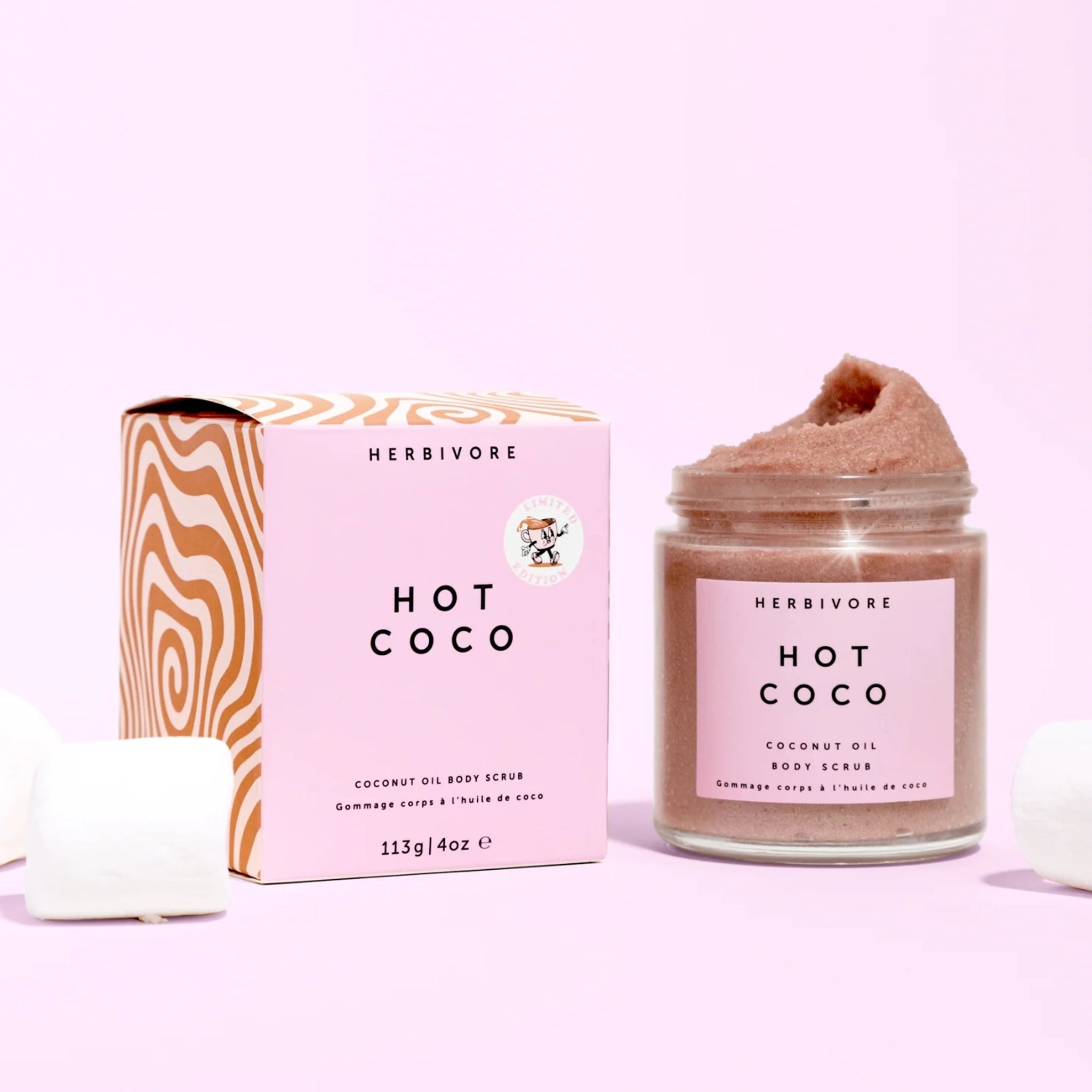 On a pink background is a hot chocolate scrub in a clear container with pink square label and black text that reads, "Hot Coco". 