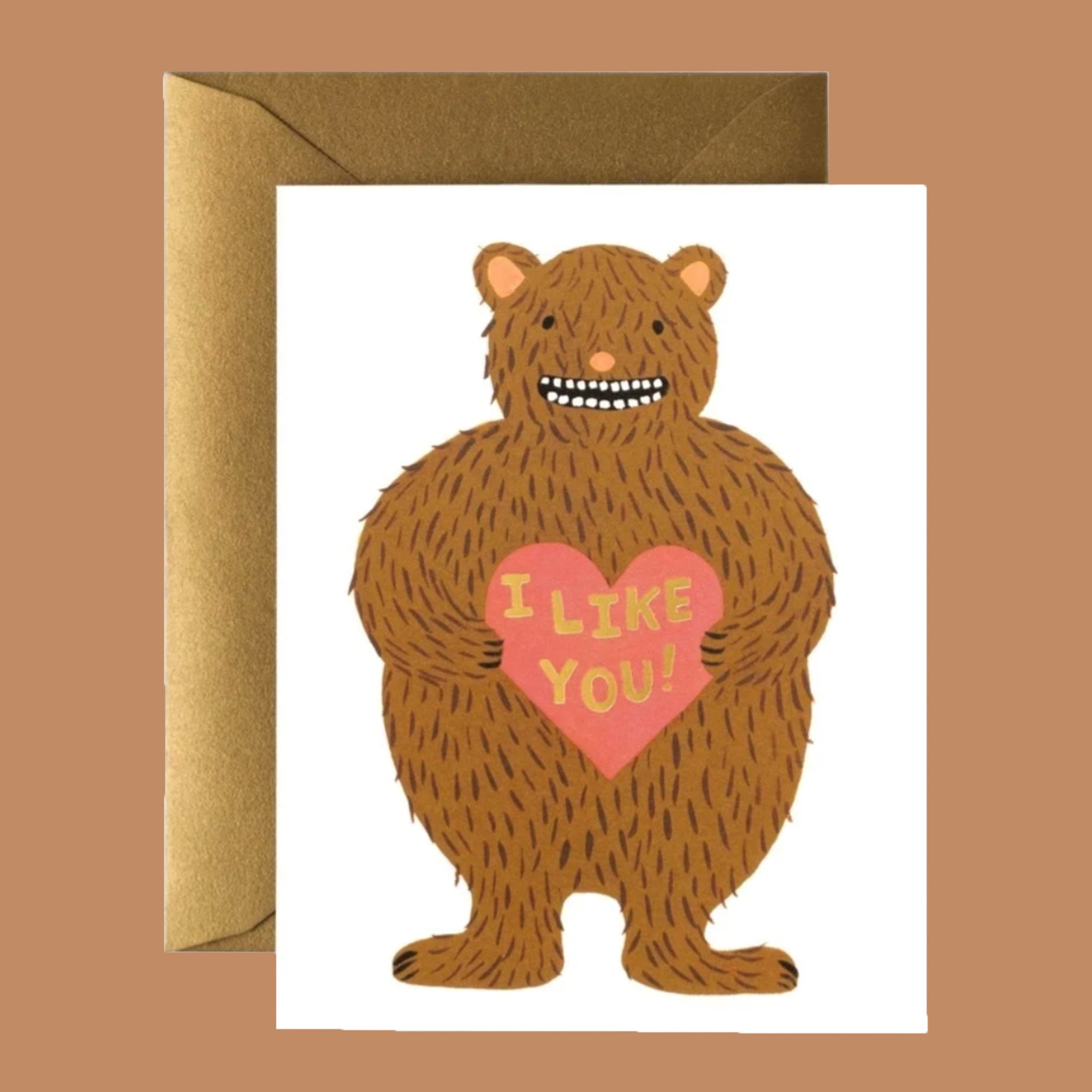 A white folded card with a brown bear graphic on the front holding a pink heart that says, "I Like You" in black writing.
