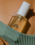 A clear packaging of body oil with a white lid and black text that reads, "In The Buff".