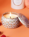 An orange and white tin that contains a single wick candle along with a circle label in the center of the lid that reads, "Voluspa Italian Bellini".