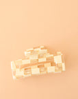 On a peachy background is an ivory and clear checker print claw clip with a rectangle shape.