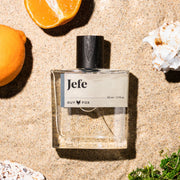 A clear bottle of cologne with a black wooden cap and a neutral label that reads, 'Jefe'.