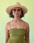 On a cream background is a model wearing a light honey colored straw sun hat with a tan ribbon around the base.
