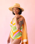 On a cream background is a model wearing a light honey colored straw sun hat with a tan ribbon around the base.