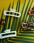 On a green background is a variety of rectangle claw clips in tortoise shades, an amber color and two different whites.